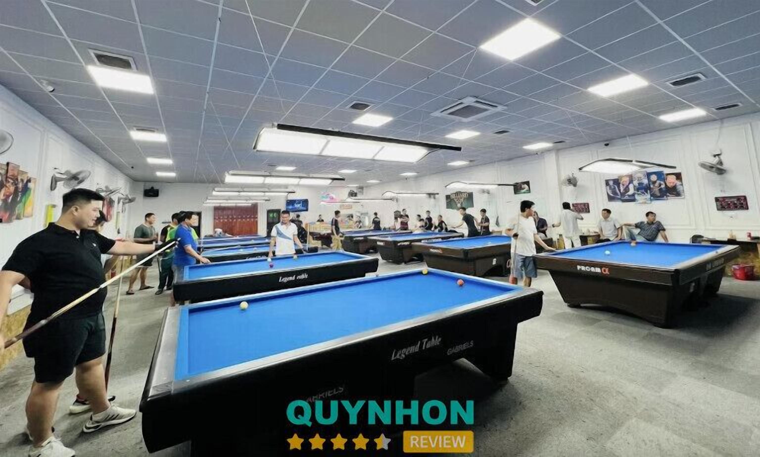 A pool hall with multiple pool tables, ceiling lights, and a few people playing.