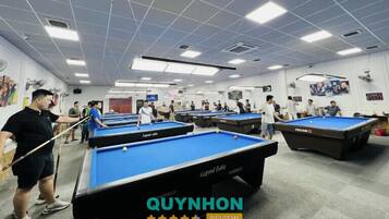 A pool hall with multiple pool tables, ceiling lights, and a few people playing.