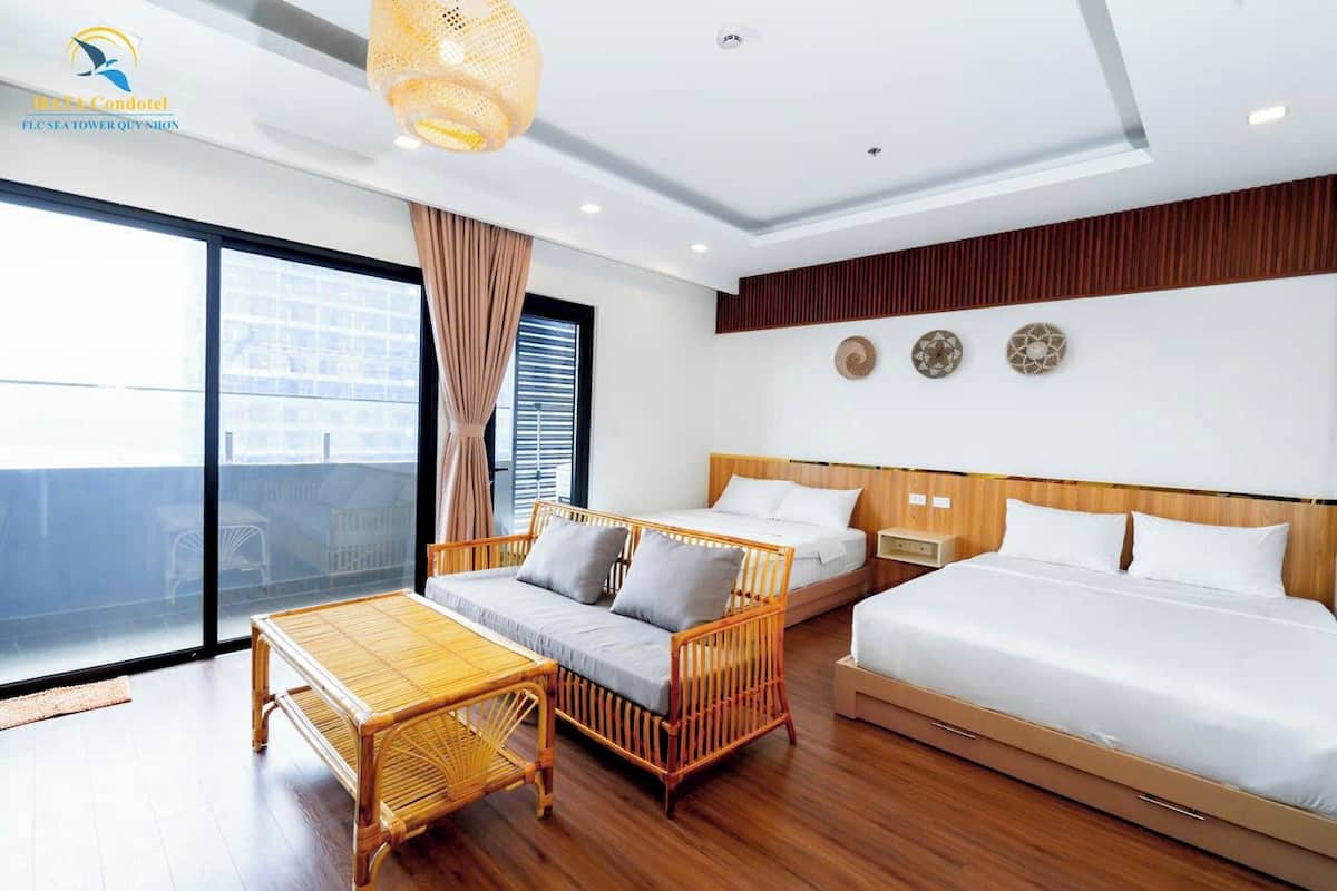 A hotel room with a large sliding glass door to the balcony, a bed, a sofa, a small table, and a hanging light fixture.
