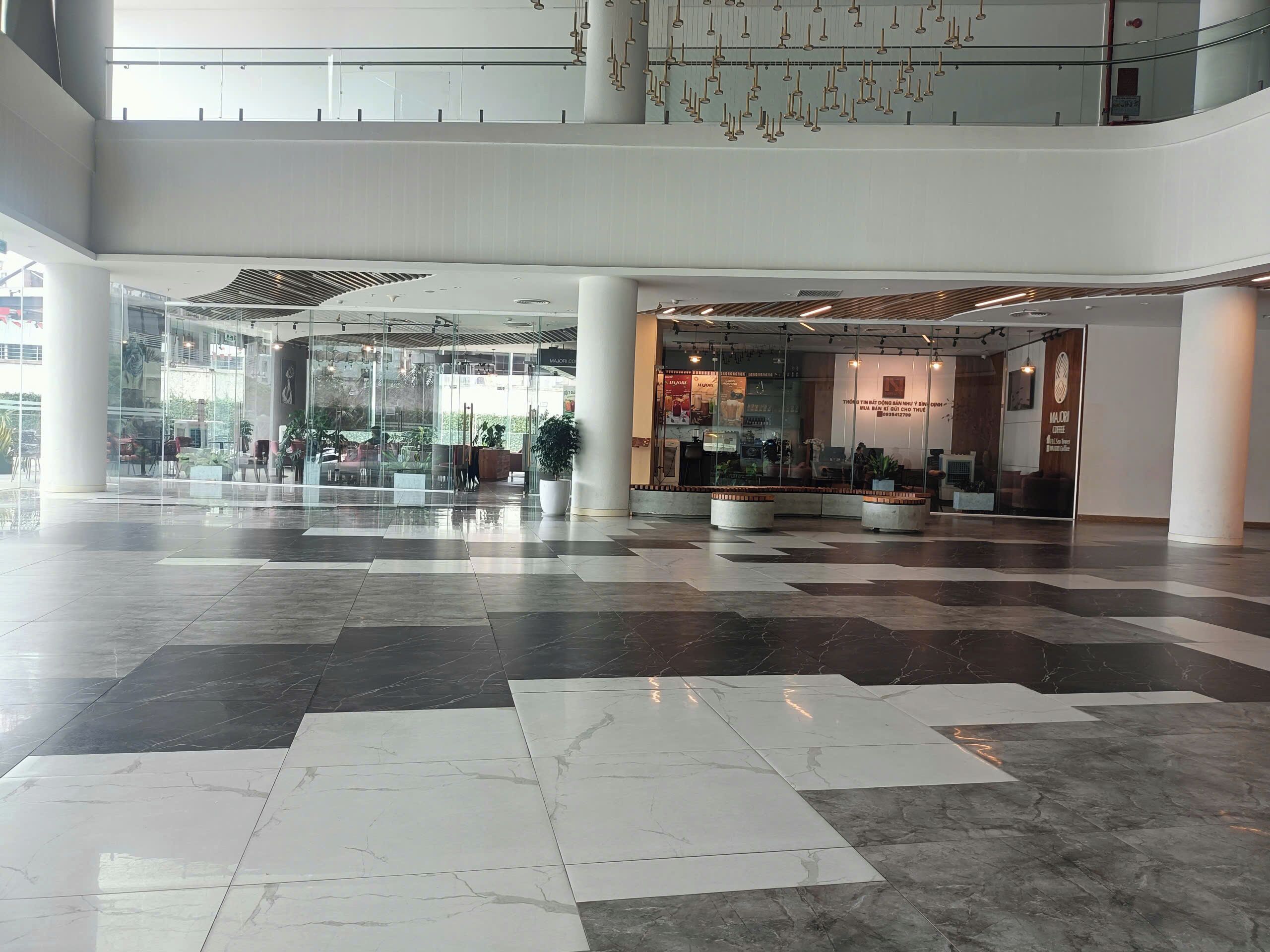 A spacious lobby with a checkered floor pattern, glass entrance, and a coffee shop.