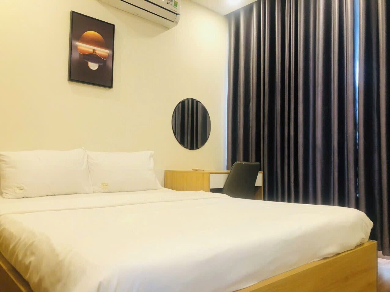 Una habitación de hotel con una cama, un escritorio, una silla, un espejo redondo y una ventana con cortinas.