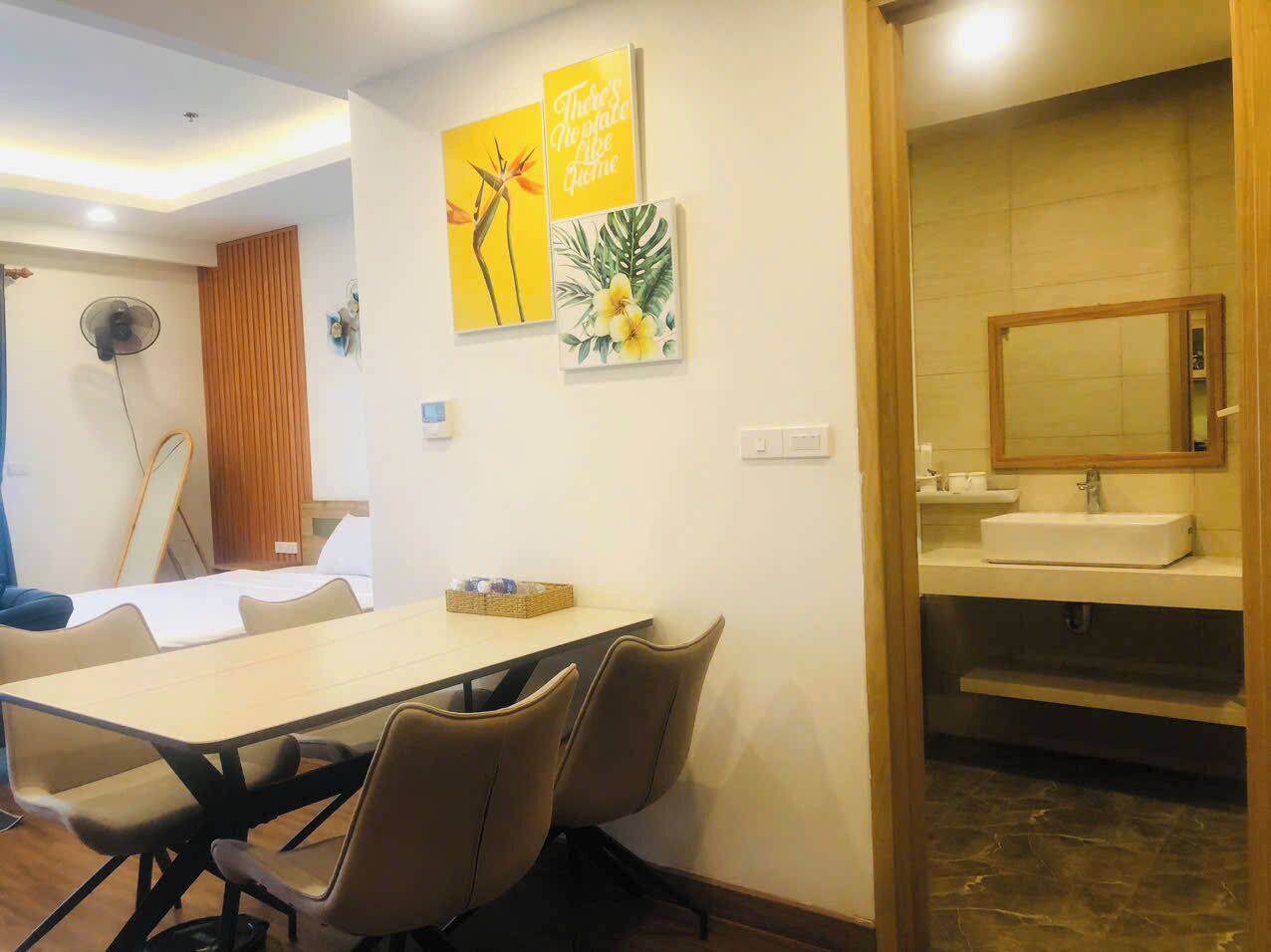 Habitación de hotel con zona de comedor que incluye una mesa y sillas, una puerta de madera y un baño con lavamanos y espejo.