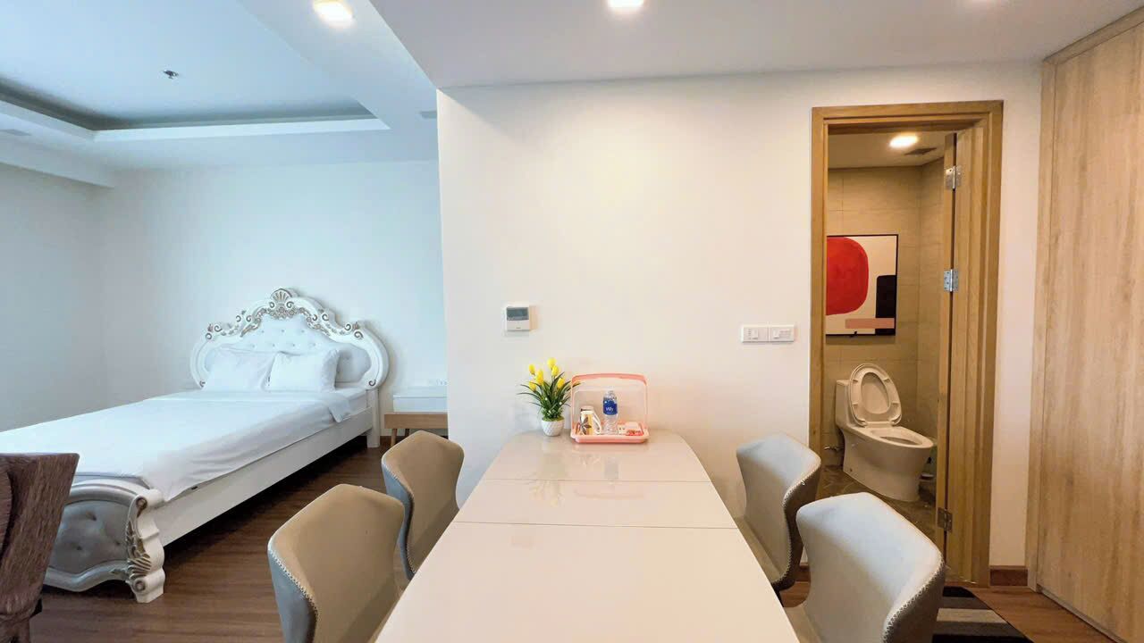 A hotel room with a single bed, a dining table with chairs, a small table with a vase and a tray, and a wooden wardrobe.