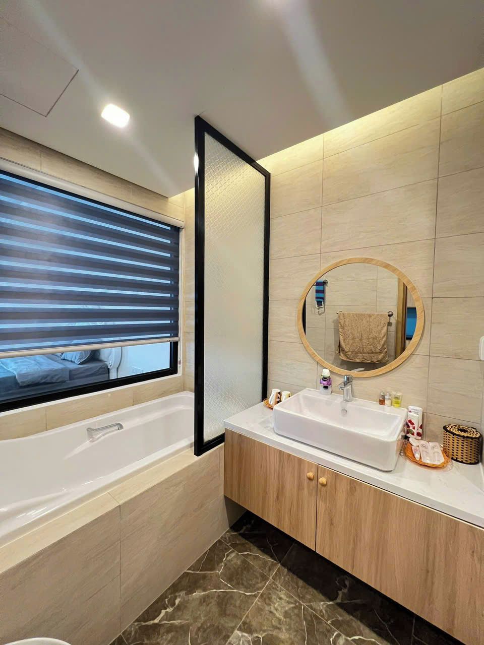Un baño moderno con bañera, lavamanos con espejo y ventana con persianas.
