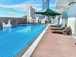Una piscina sul tetto con galleggianti a forma di cigno, lettini e un ombrellone verde.