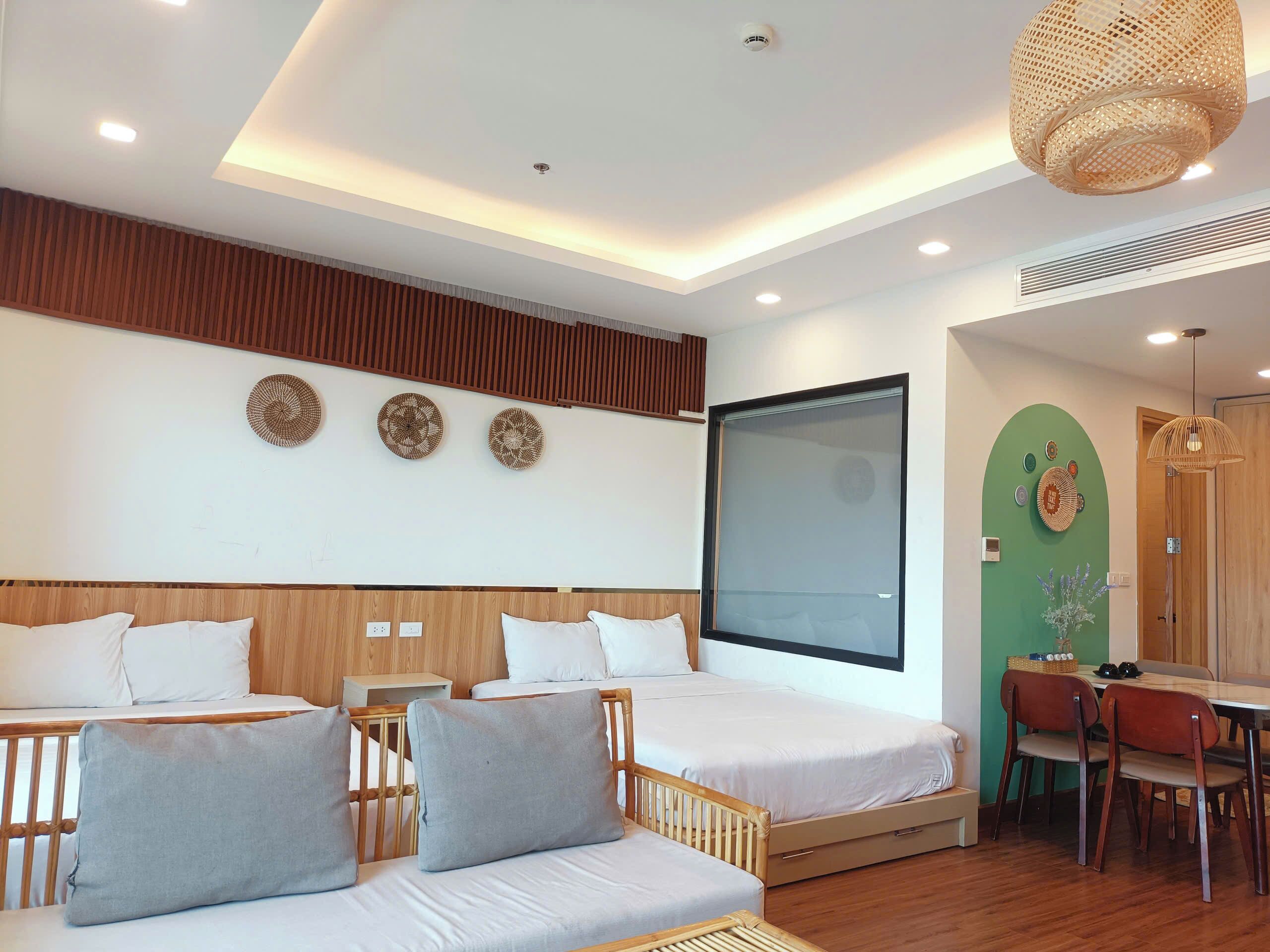 A modern hotel room with two beds, a dining area, and a large window.