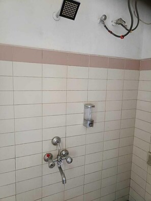A tiled shower area with a handheld showerhead and a soap dispenser. - SPACE4 RESORT (Ooty)