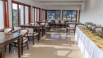 A dining area with multiple tables and chairs, large windows, and a buffet line with food containers.
