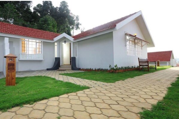 A two-story house with a tiled roof, a paved driveway, and a small lawn area.