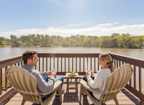 Two people sitting on deck chairs facing a lake with a wooden railing and a small table with food and drinks. - Lakefront Retreat - Close to RAFB, Pets & Kids Friendly (Warner Robins)