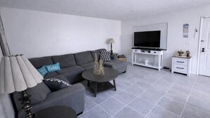 Un salon moderne avec un canapé gris, une table basse, un meuble pour la télévision et un petit meuble de rangement.