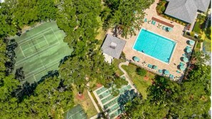 Vue aérienne d’une propriété dotée d’un court de tennis, d’une piscine et d’un patio couvert.