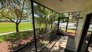 Un balcon fermé offrant une vue sur un espace paysager et un parking.