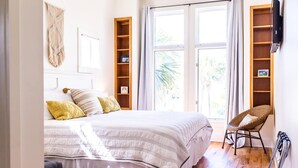 A bedroom with a large bed, a wooden chair, a macrame wall hanging, and a window with curtains. - Days Like This -spacious Home Steps From the Beach (Navarre)