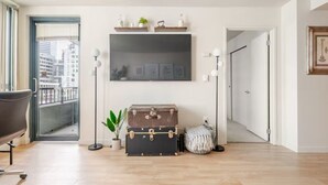 Un salon moderne avec un grand téléviseur à écran plat fixé au mur, une valise ancienne, une plante en pot et un lampadaire.