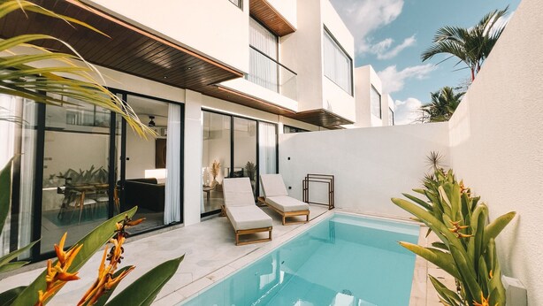 Une maison moderne dotée d’une piscine, de chaises longues et de plantes tropicales.