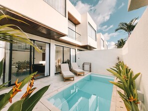 Une maison moderne dotée d’une piscine, de chaises longues et de plantes tropicales.