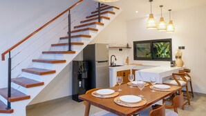 Une cuisine moderne dotée d’un îlot central intégré, d’un coin repas avec une table et des chaises en bois, et d’un escalier avec des marches en bois et une rampe en métal.