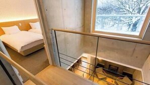 A modern room with a bed, a wooden staircase, and a view of a snowy landscape through a window. - Mizunara Chalet by Elite Havens (Kutchan)