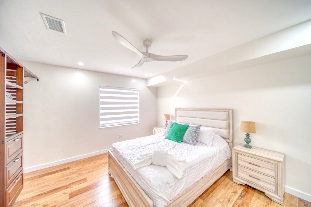 A bedroom with a bed, a ceiling fan, a nightstand, a dresser, and a window with blinds.