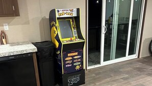 En Pac-Man-spelautomat står i ett rum med en köksbänk, en papperskorg och en skjutdörr i glas som leder ut.