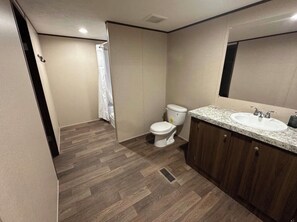 Ein Badezimmer mit Holzboden, Toilette in Weiß, einem Waschbecken mit Spiegel und einer Duschvorhang.
