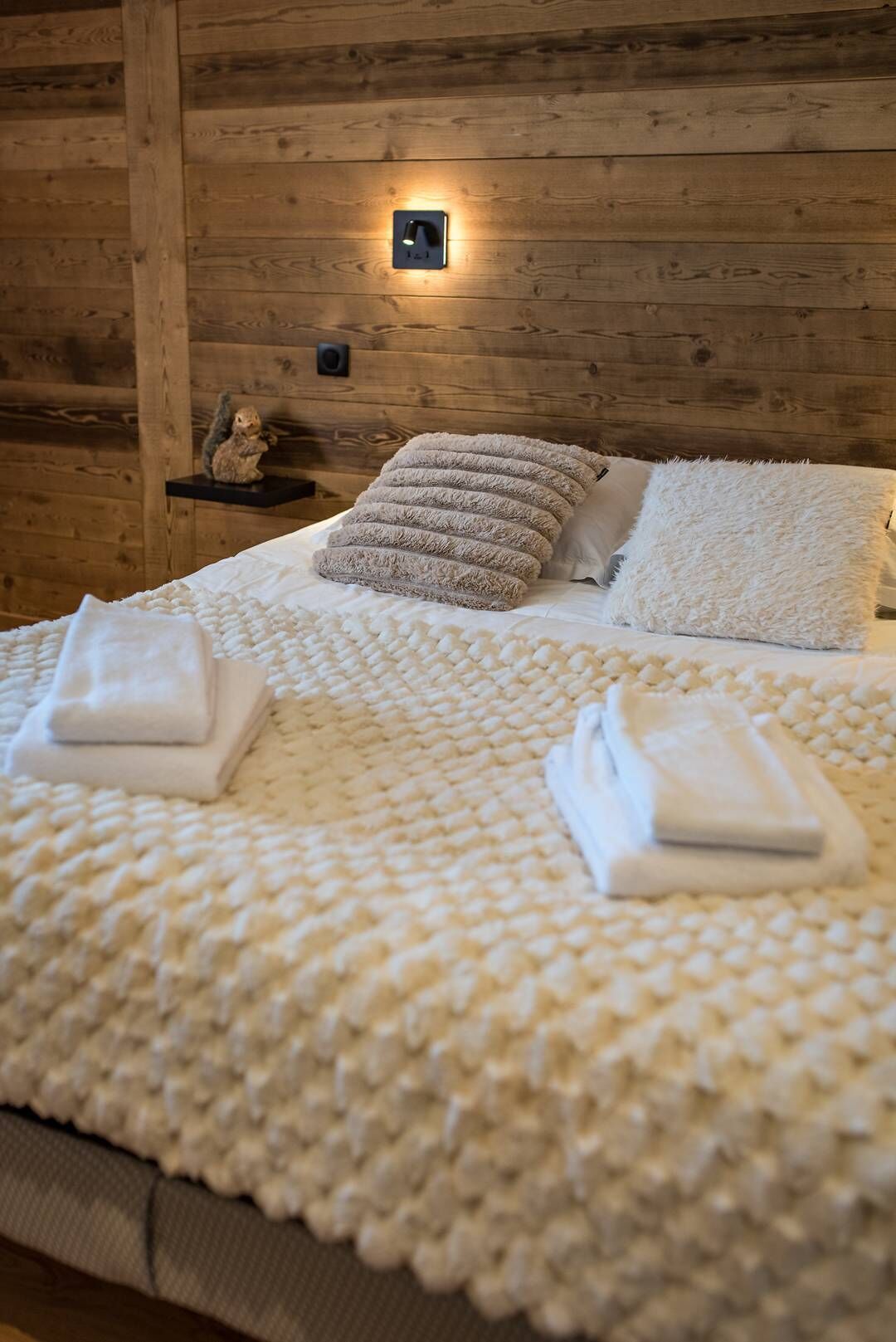 Un dormitorio acogedor con pared de madera, una cama con almohadas mullidas y una pequeña estantería con una figurita de ardilla.