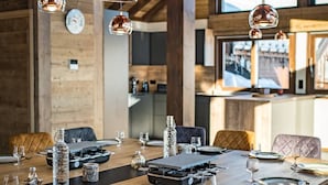 A dining area with a wooden table set for a meal, surrounded by chairs, and overhead pendant lights.