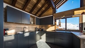 A modern kitchen with dark cabinetry, a wooden ceiling, and a large window offering a view of a snowy landscape.