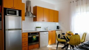 A compact kitchen with wooden cabinets, a refrigerator, a microwave, and a dishwasher. There is a dining area with yellow chairs and a table. - A beautiful 2 bedroom apartment with sea views and hot tub .  (Pegeia)