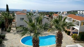 A pool surrounded by palm trees and buildings with solar panels. - A beautiful 2 bedroom apartment with sea views and hot tub .  (Pegeia)