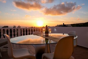 A round glass table with four chairs, a bottle of wine, and glasses on a terrace with a sunset view. - A beautiful 2 bedroom apartment with sea views and hot tub .  (Pegeia)