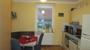 A compact kitchen with a dining area, featuring a window with a view, a radiator, and basic appliances. - Vacation apartment near the old town and lake (Neubrandenburg)