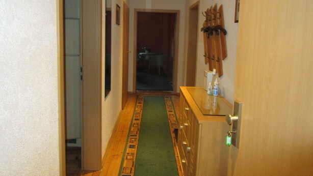 A narrow hallway with a patterned carpet, wooden cabinets, and a coat rack. - Vacation apartment near the old town and lake (Neubrandenburg)
