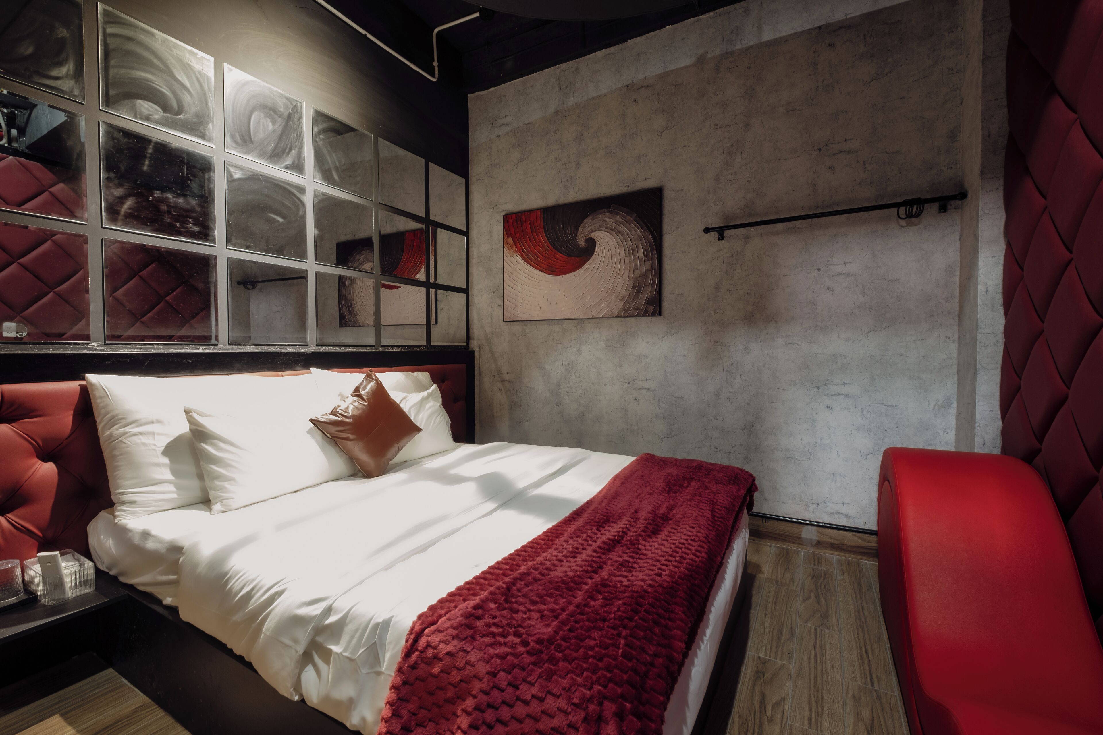 Un dormitorio moderno con una cama grande, una silla roja y una pared de concreto con un cuadro.