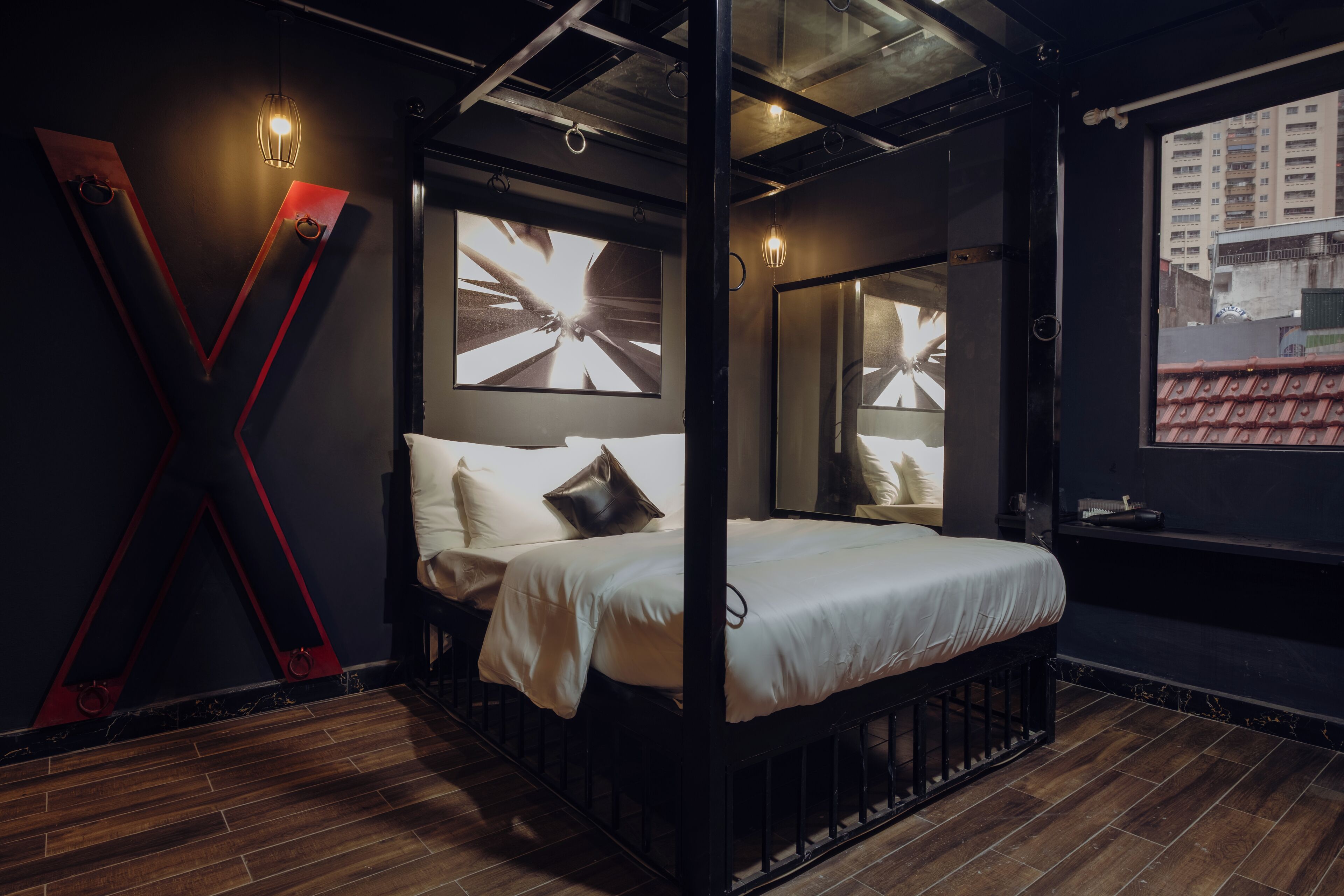 Een moderne slaapkamer met een bed, een groot V-vormig lamparmatuur en uitzicht op een stadsgezicht door een raam.