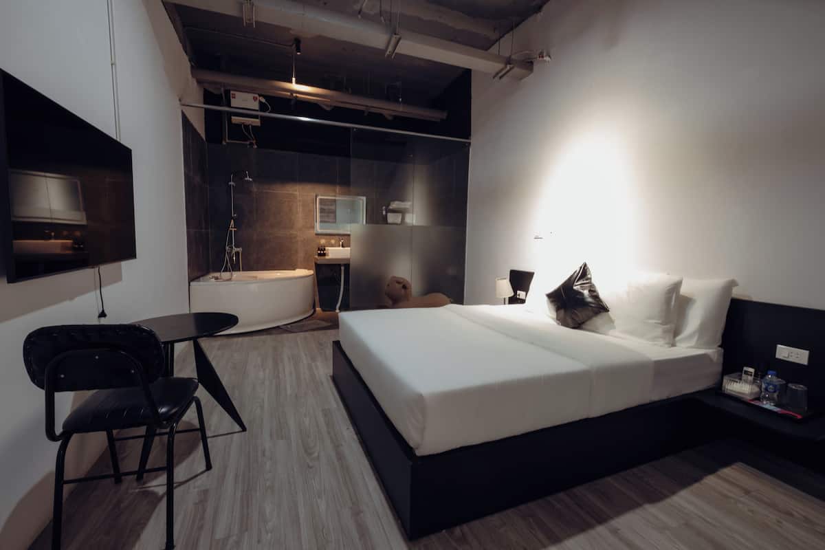 Habitación de hotel moderna con cama, escritorio y zona de ducha.
