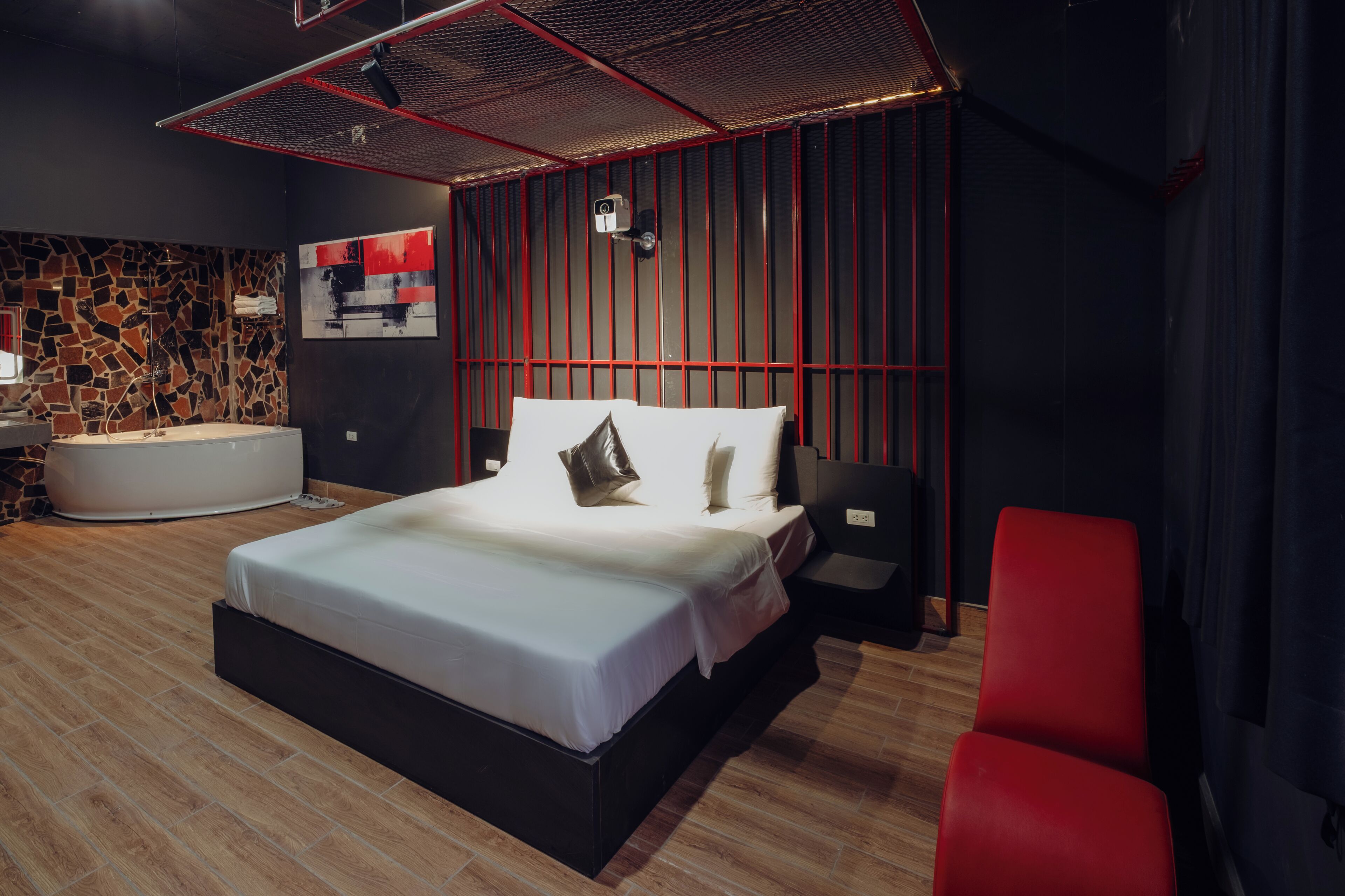 A modern bedroom with a large bed, a red chair, a stone wall, and a red ceiling.