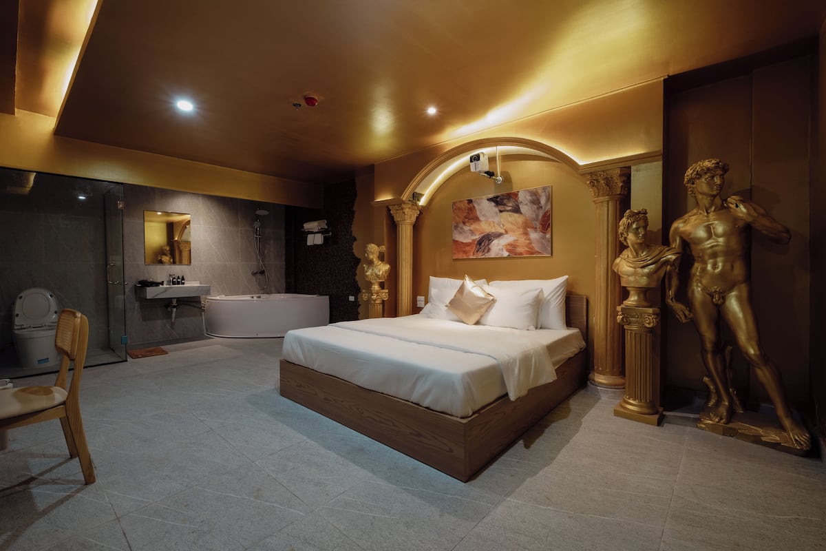 Un dormitorio moderno con una cama grande, una zona de estar, un baño y una estatua de un hombre.