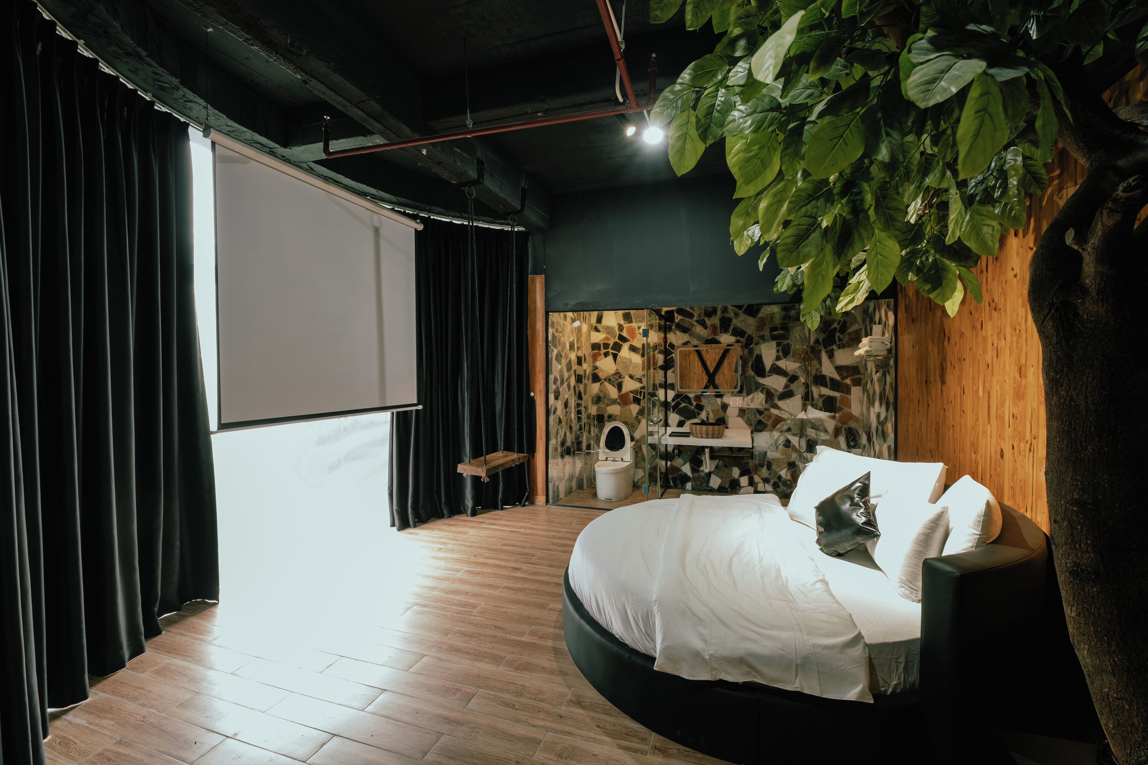 A modern bedroom with a curved bed, a stone wall, and a large plant.