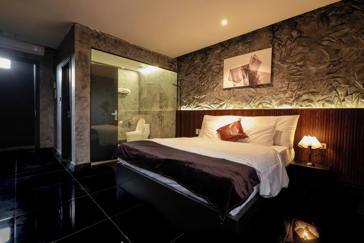 Una habitación de hotel moderna con una cama grande, cabina de ducha con paredes de vidrio y pared con textura de piedra.