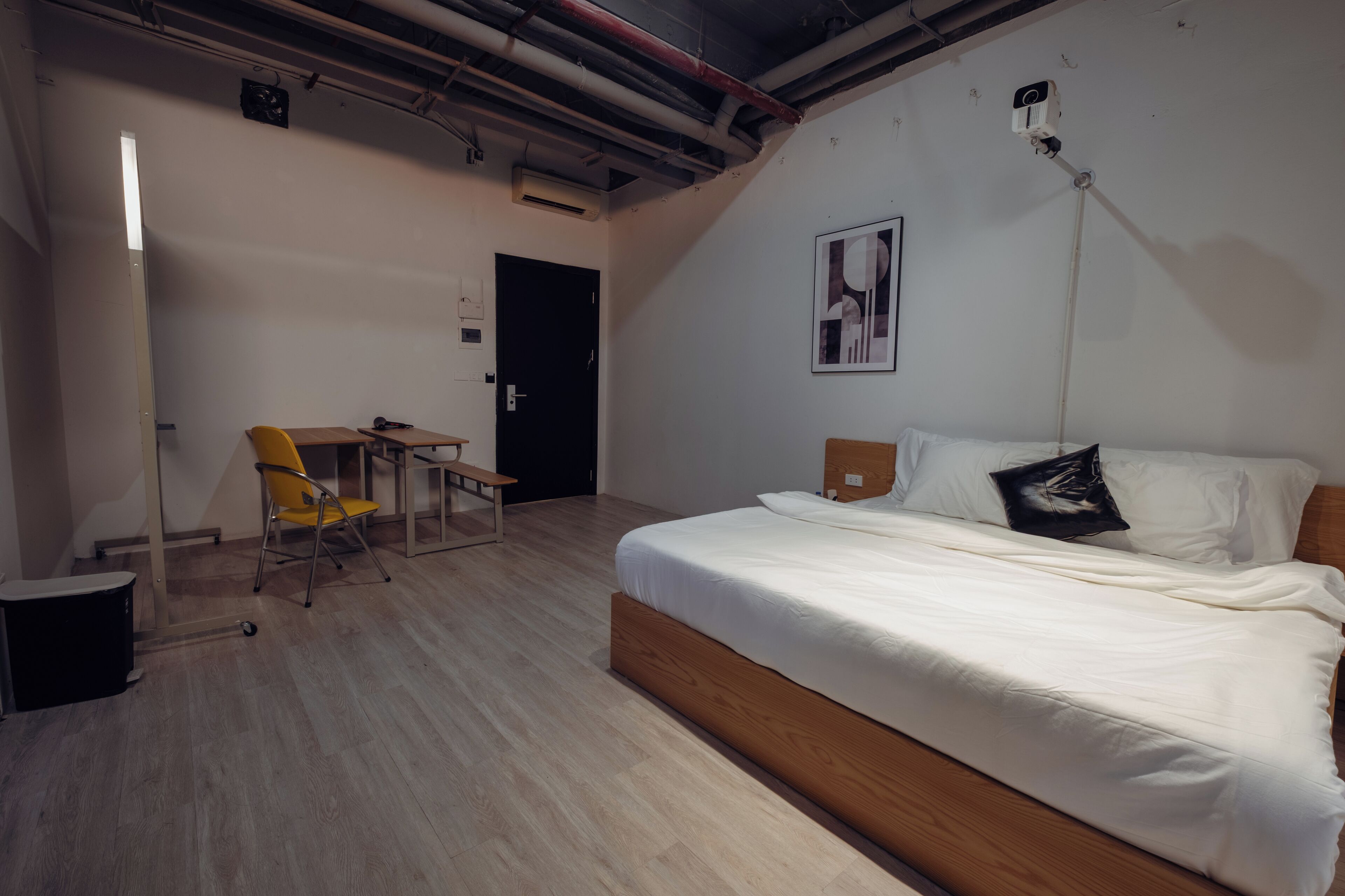 A bedroom with a wooden bed, a desk, a chair, and a small trash bin.
