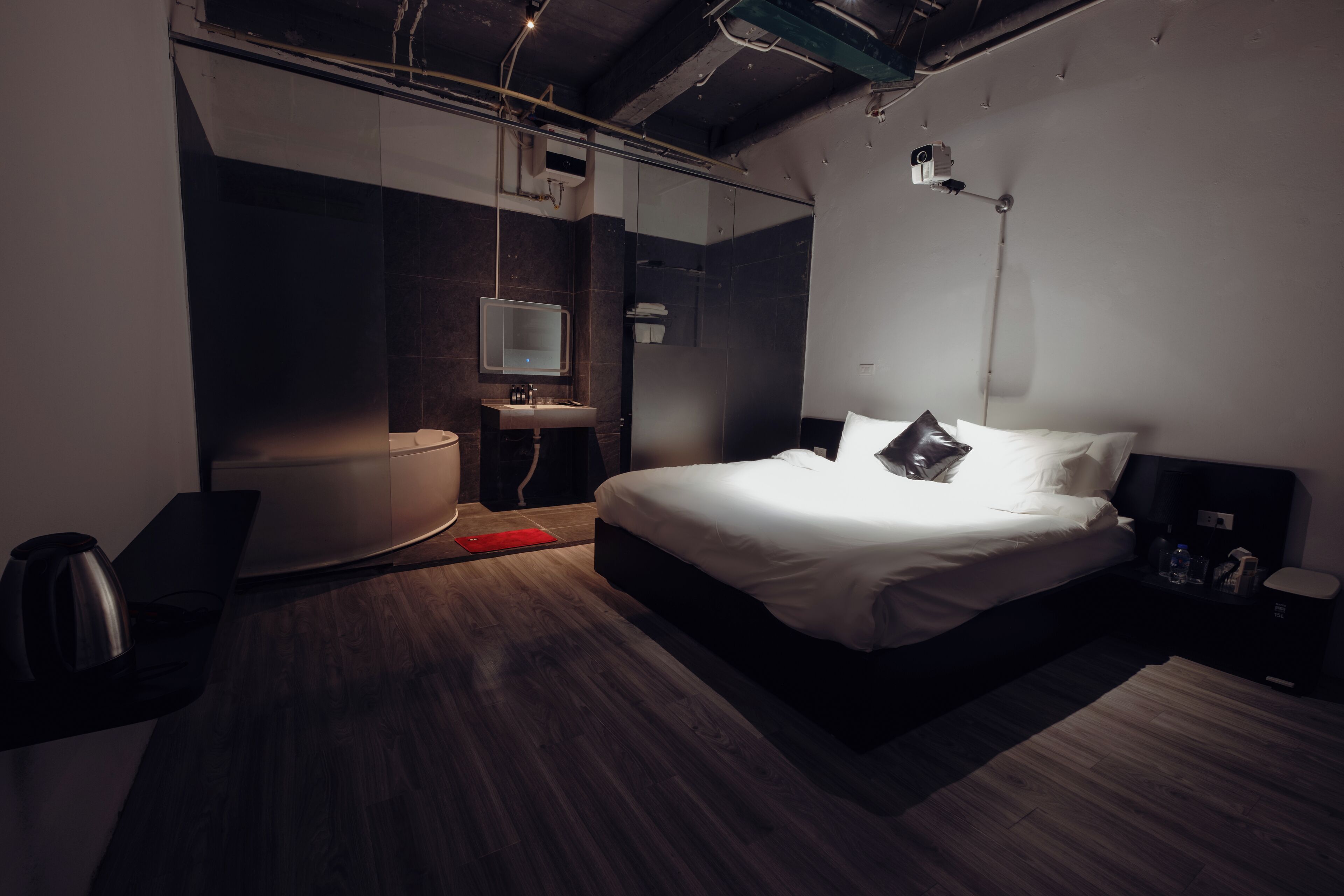 Een moderne hotelkamer met een groot bed, een nachtkastje, een spiegel, een kleine badkamer met een wastafel en een rood vloerkleed.