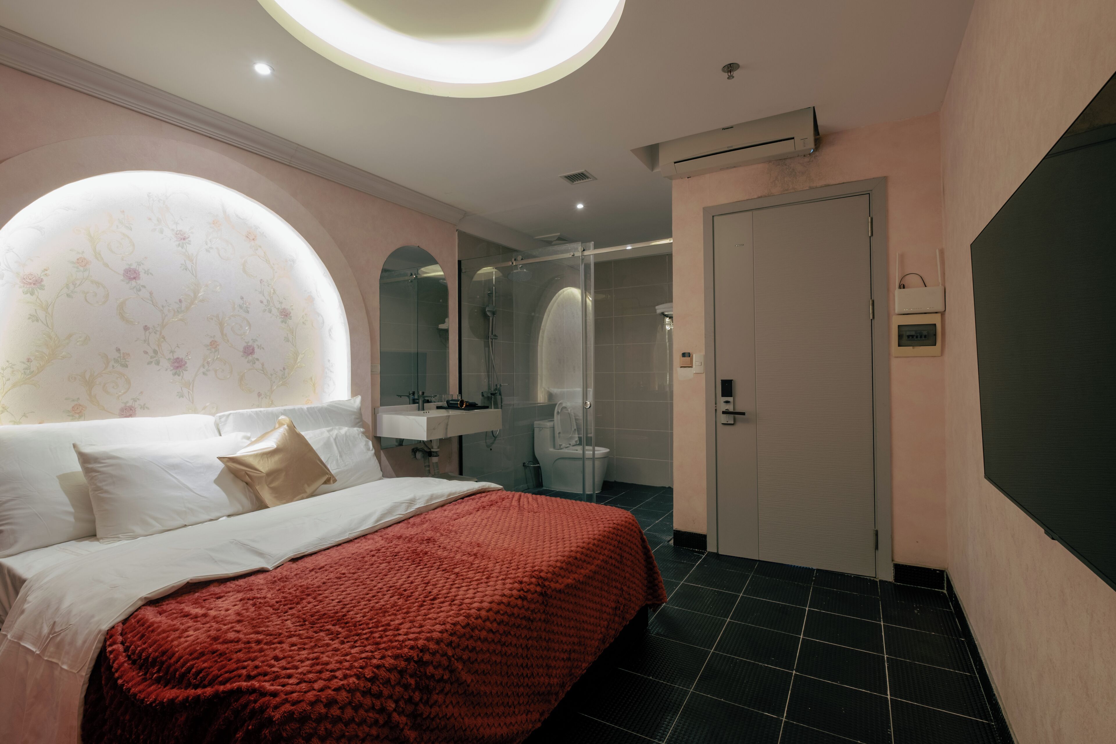 Une chambre d’hôtel moderne dotée d’un grand lit, d’une salle de bain avec une douche en verre et d’un puits de lumière circulaire.