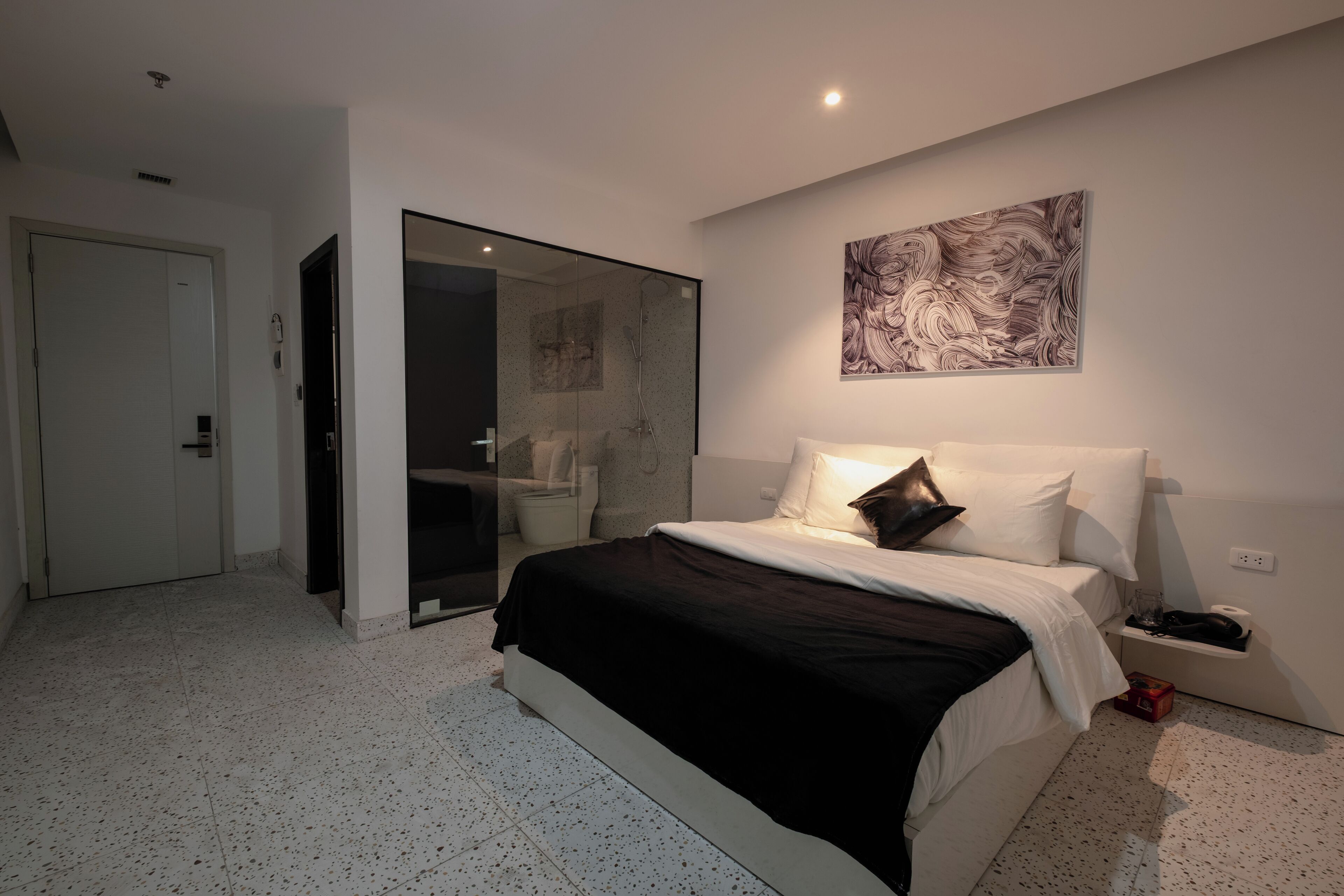 A modern bedroom with a large bed, a glass shower enclosure, and a wall-mounted artwork.