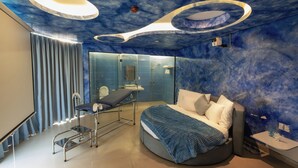 A modern bedroom with a circular bed, a glass partition, a bedside table, and a ceiling with circular light fixtures. - Love in the Atlantis Hotel (Hanoi)