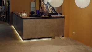A reception desk with a modern design, featuring a wooden counter and a large mural on the wall behind it. - Love in the Atlantis Hotel (Hanoi)
