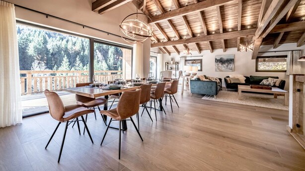 Un comedor amplio con techo de madera y grandes ventanales con vistas a una zona boscosa.