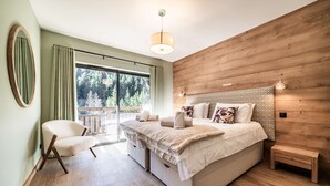 Un dormitorio moderno con una cama grande, un cabecero de madera, una mesita de noche, una silla y vistas a árboles a través de una puerta corredera.