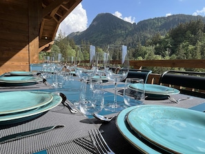 Une table à manger dressée avec des assiettes, des couverts et des verres à vin, donnant sur un paysage montagneux.